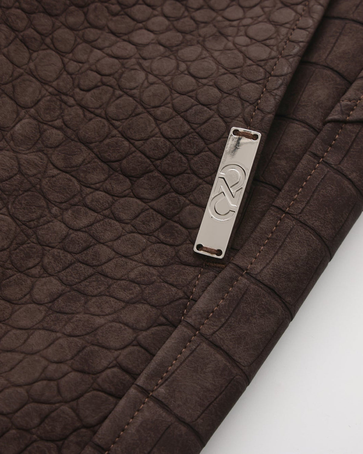 Close-up of the silver-tone BSZN side plaque on the reptile-embossed brown shorts