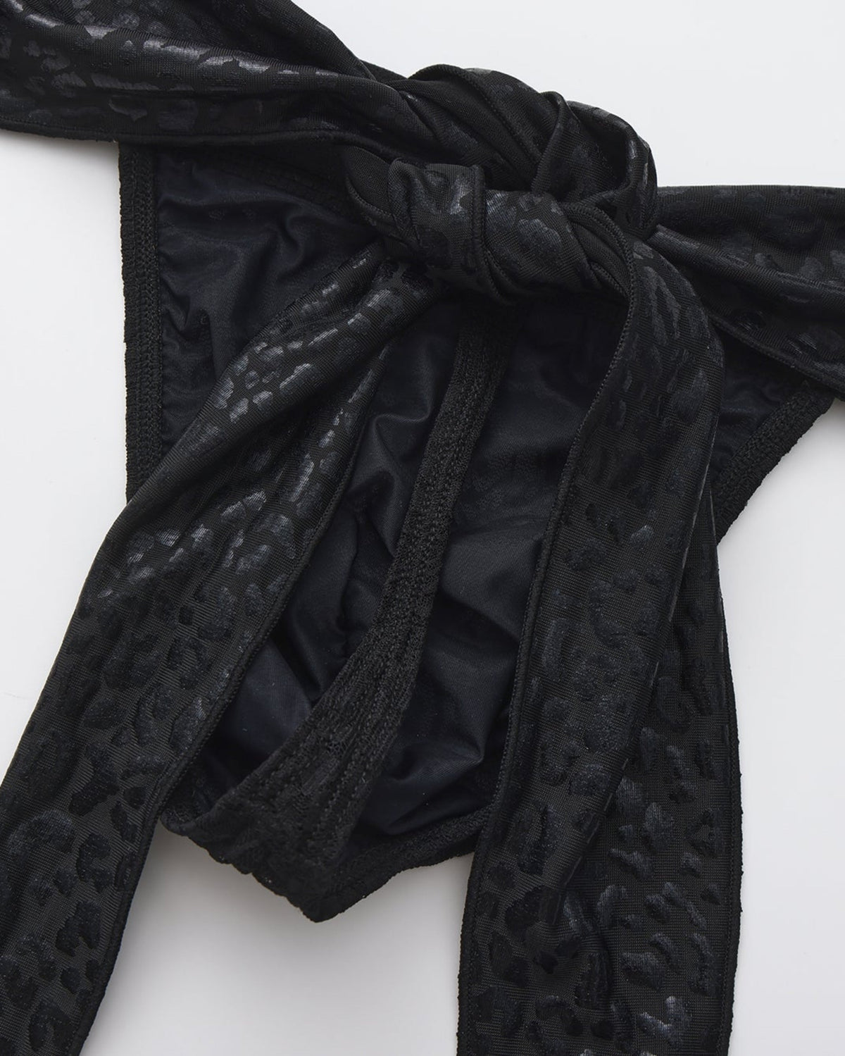 BSZN Glossy black scarf ties knotted at the waist, close-up.
