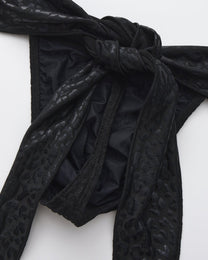 BSZN Glossy black scarf ties knotted at the waist, close-up.