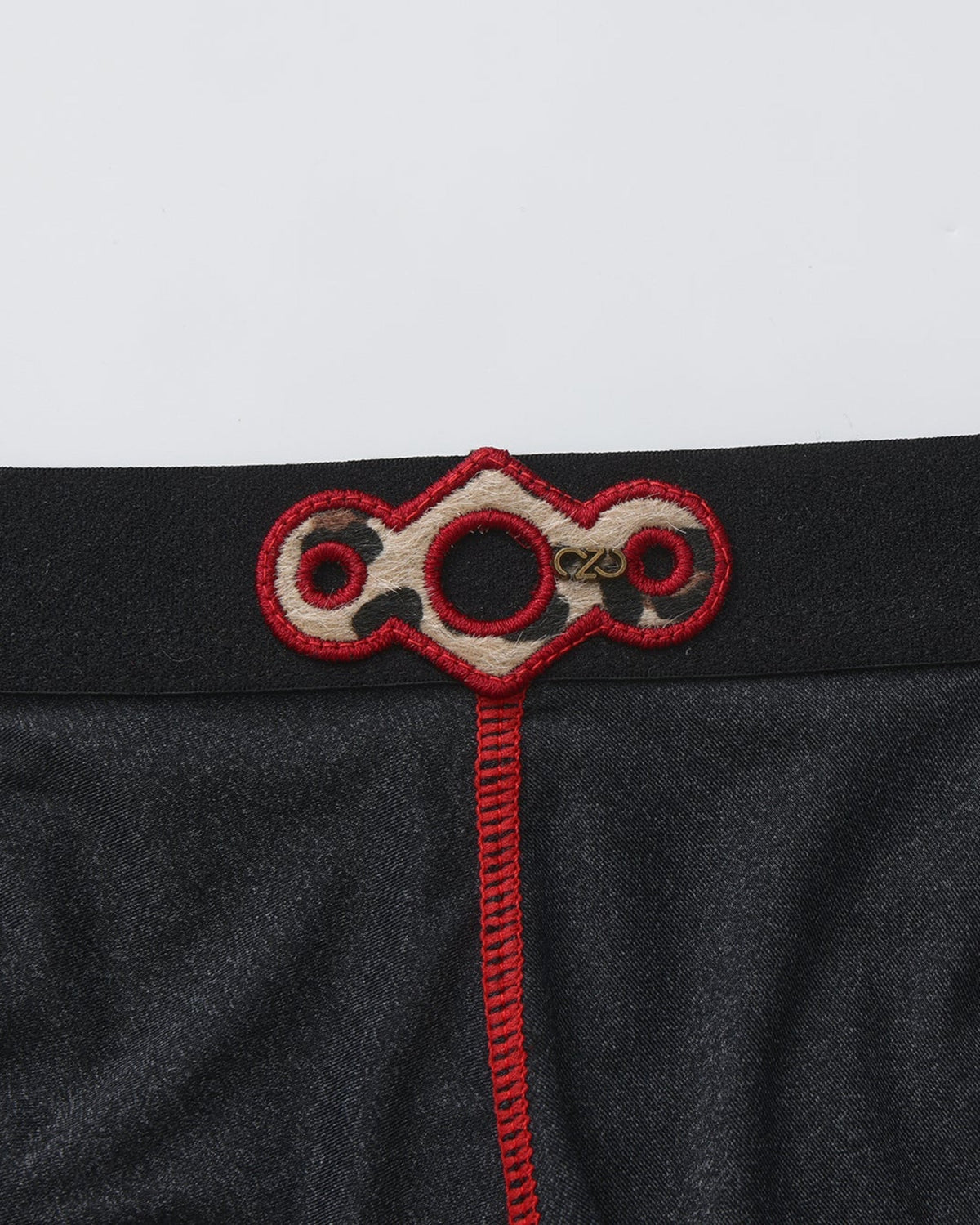 BSZN Spiderweb Heart Cutout Brief — Metal emblem and red embroidery close-up.